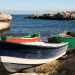 Le tipiche barche dei pescatori, colorate di verde e rosso o bianco e blu, sono ormeggiate su una spiaggia di pietre e ciottoli chiari che si stempera in un meraviglioso mare blu